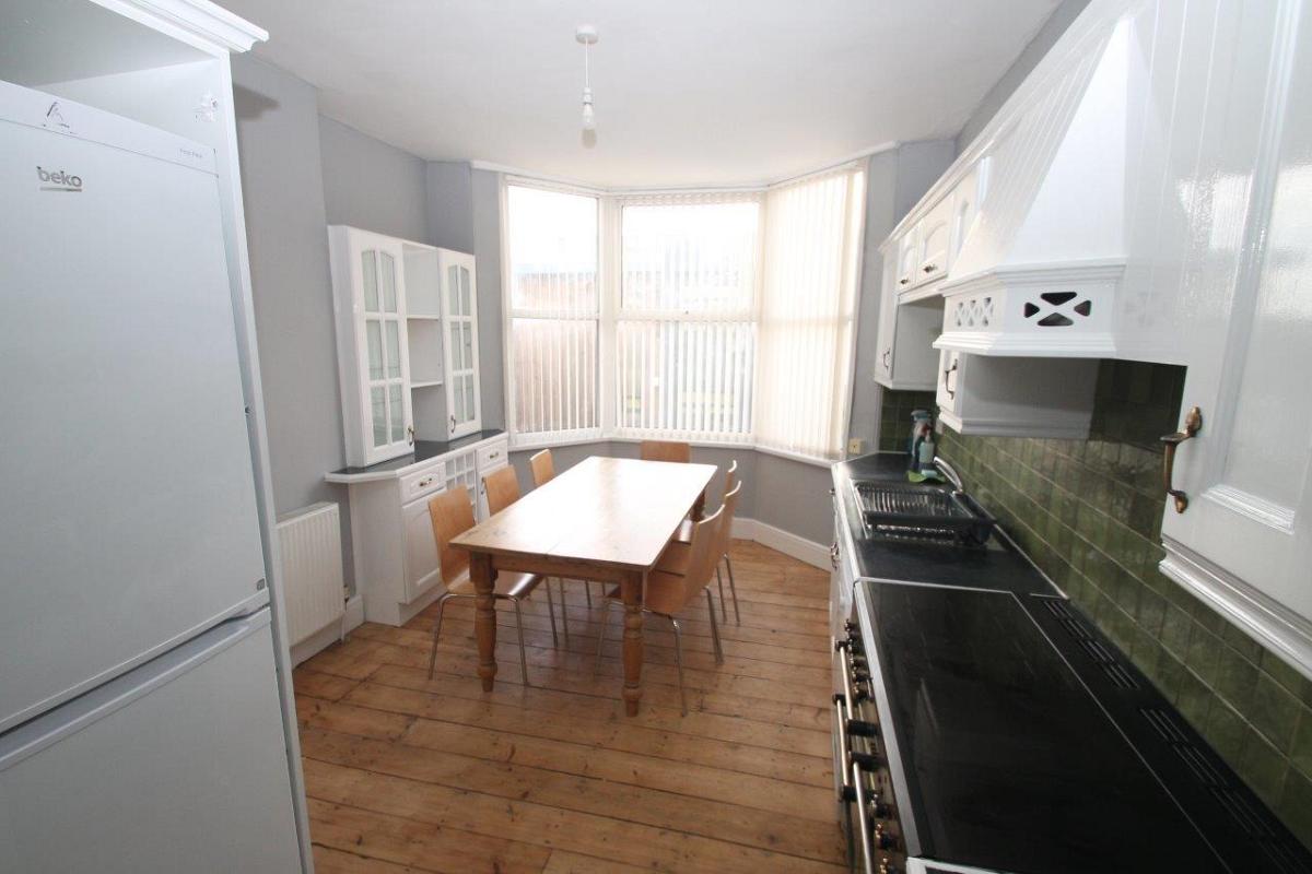 Green tiled shared kitchen with dining table and white display cabinet