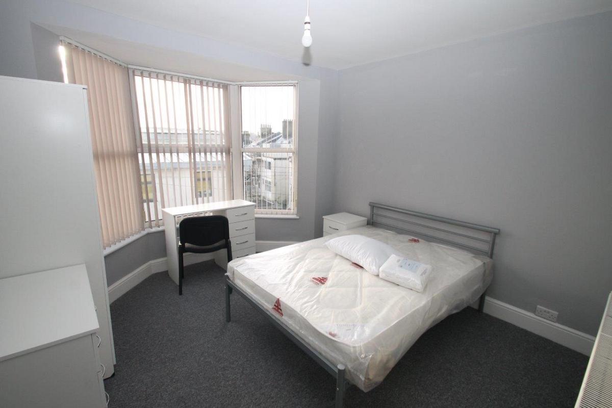 Student bedroom with double bed, two door wardrobe, chest of drawers, bedside table and desk in front of large bay window