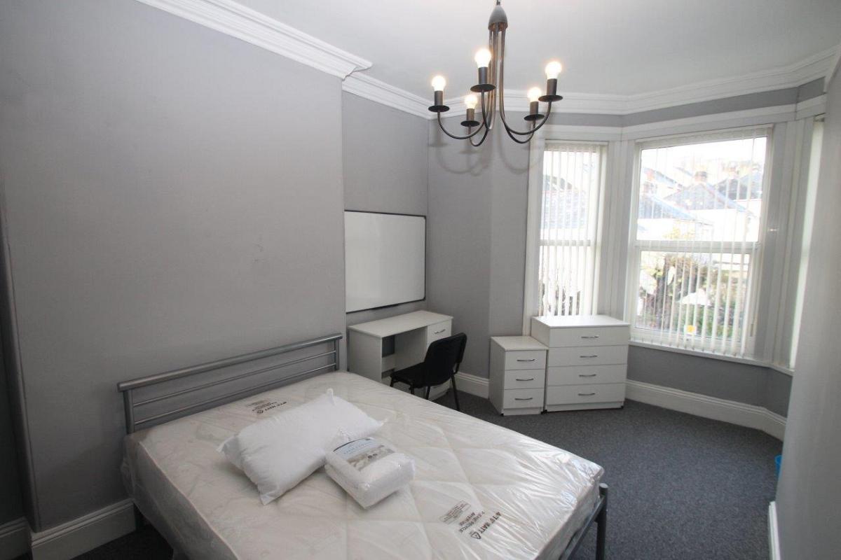 Student bedroom with double bed, chest of drawers, bedside table, desk with whiteboard, large bay window