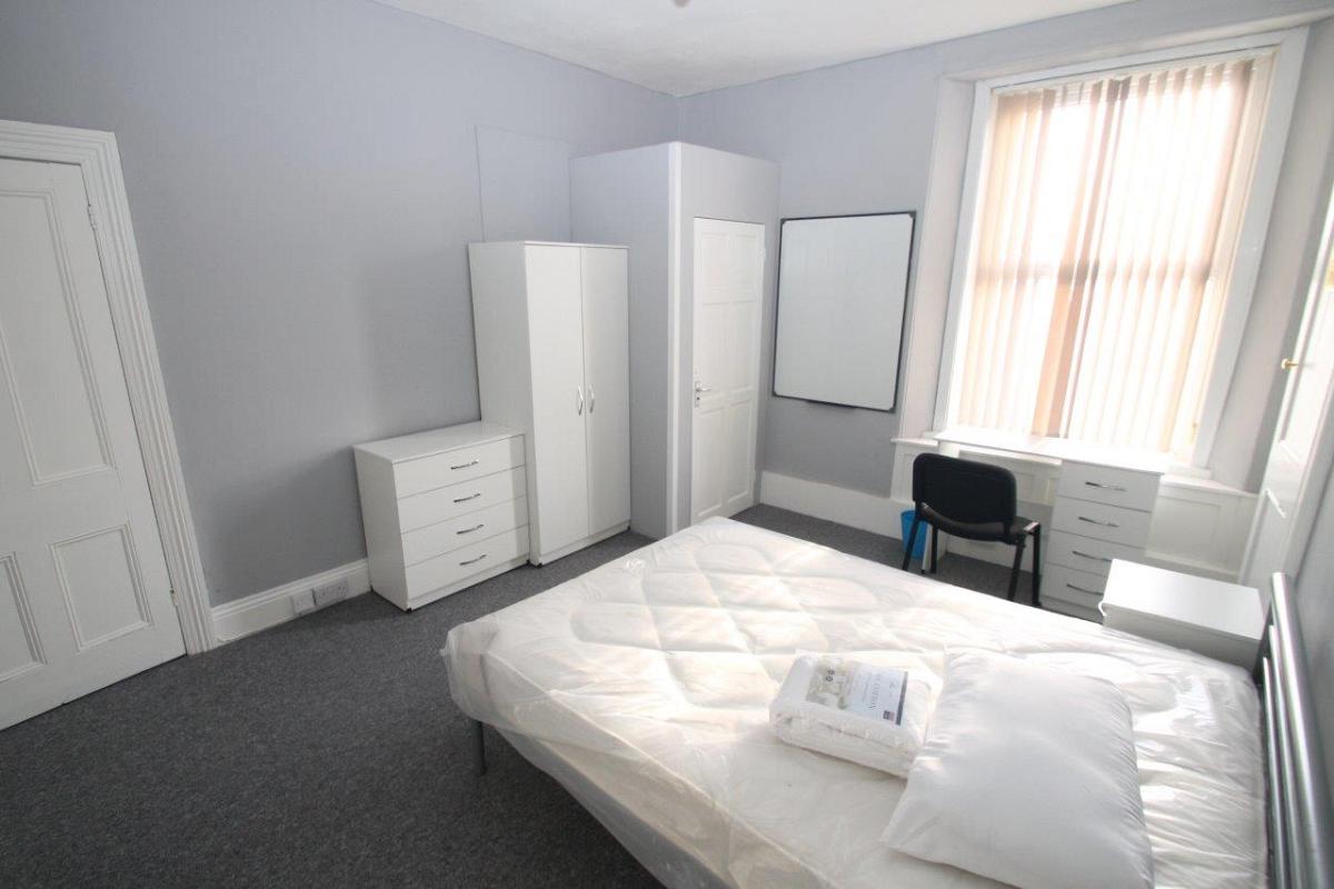 Student bedroom with double bed, chest of drawers, two door wardrobe, desk in front of window, whiteboard and door to en-suite