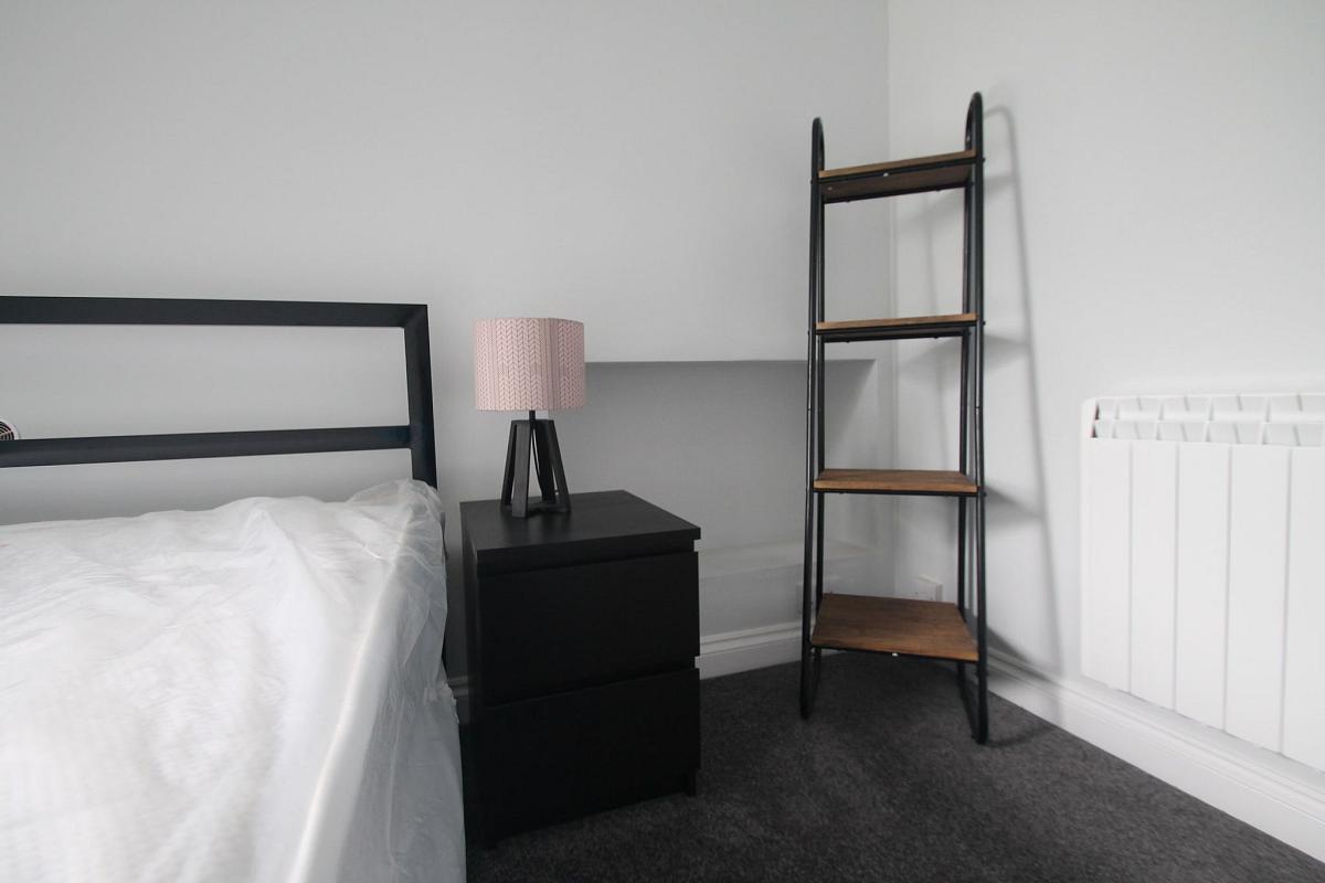 student bedroom with double bed, bedside table and shelving unit