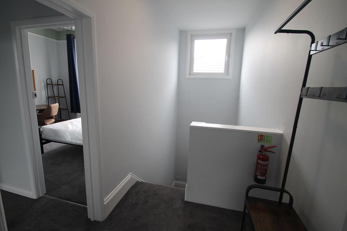 Hallway with coat rail, stairs leading down and leading to student room