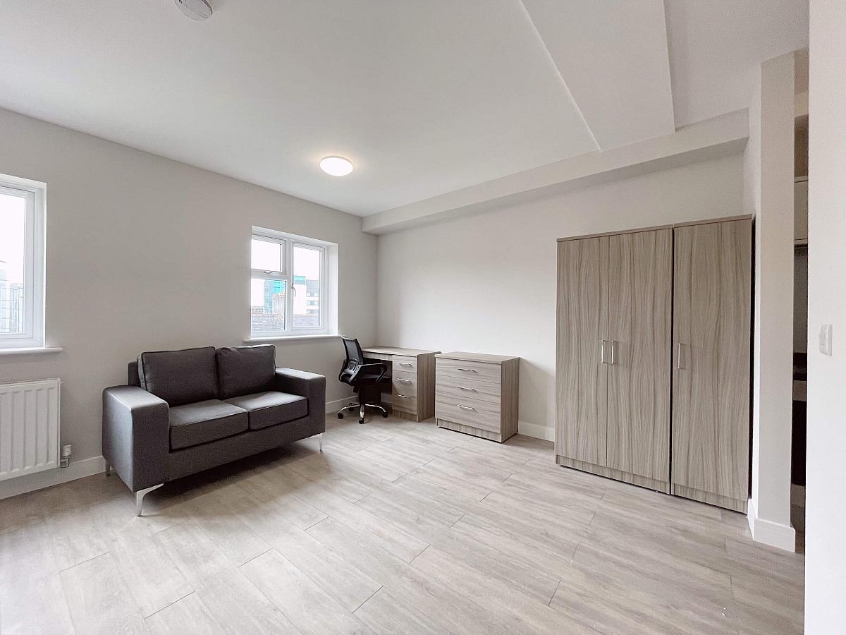 Large living space with three door wardrobe, chest of drawers, desk and two seater sofa