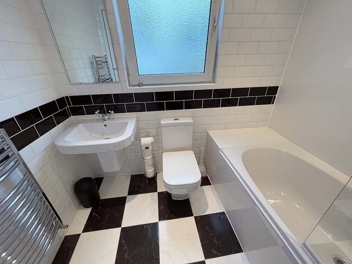 White bathroom with bath with shower facility, mirror mounted above the sink, and toilet