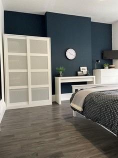student bedroom with double bed, two door white wardrobe, chest of drawers. and small table