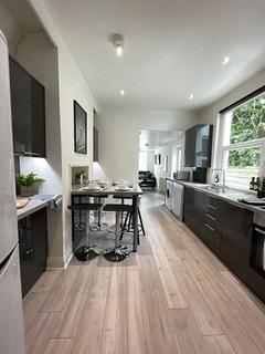 long kitchen with fridge freezer, induction hob and cooker, washing machine and dining table with four black bar stools