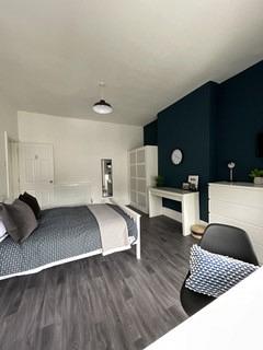 student bedroom with double bed, desk with black chair, white two door wardrobe, chest of drawers