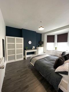 student bedroom with double bed, two door wardrobe, chest of drawers, desk with black chair in front of large bay windows