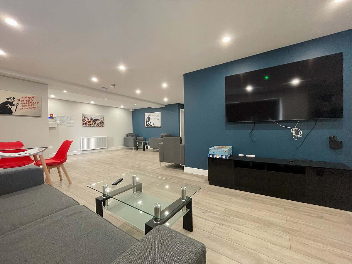 Downstairs communal area with two double sofas, three yellow arm chairs, wall mounted tv and pool table
