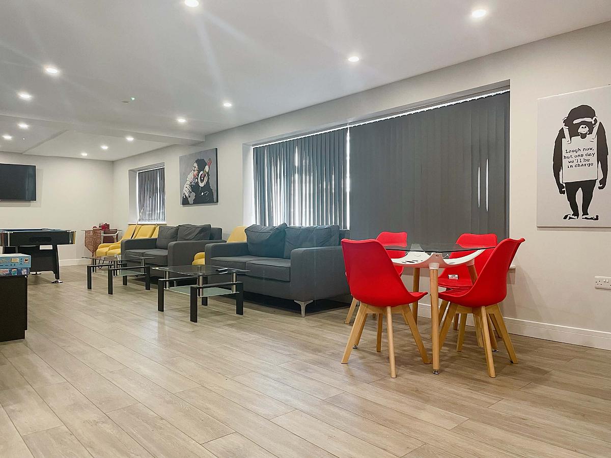 Downstairs communal area with two double sofas, four yellow armchairs, glass table with dining chairs and art on walls