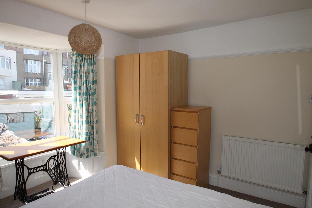 third student room with double bed, two door wardrobe, tall chest of drawers, desk in front of window facing the backgarden