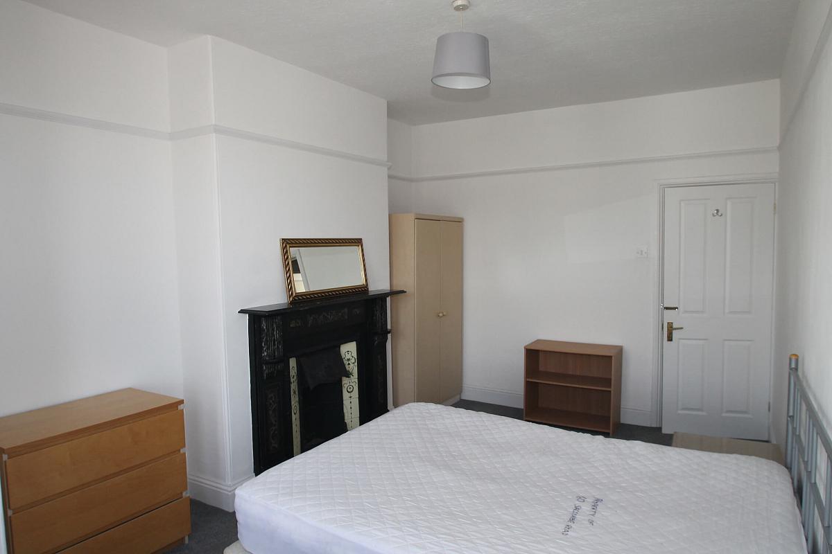 fifth student bedroom with double bed, chest of drawers, two door wardrobe, bedside table, shelving unit and mirror above fireplace