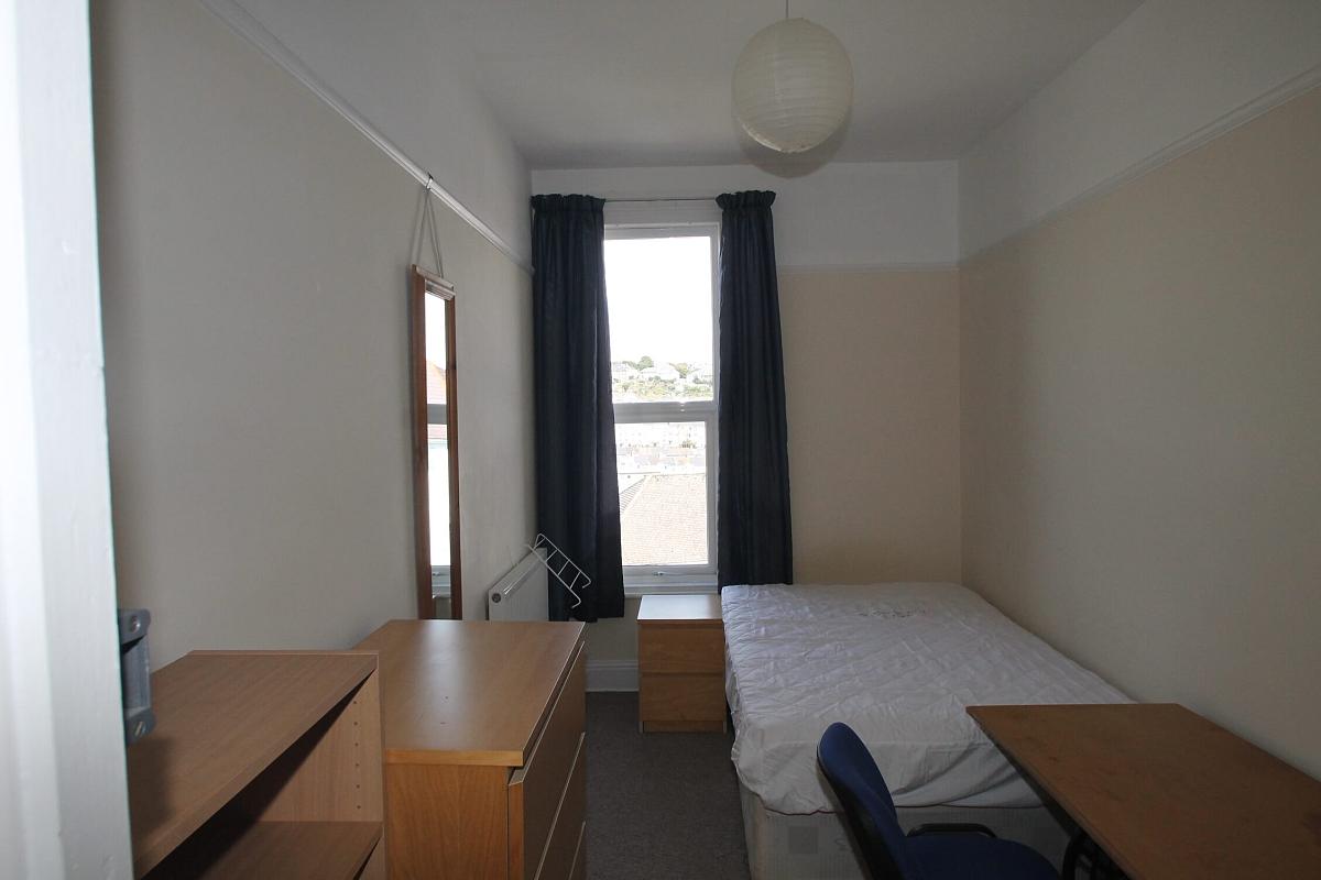 sixth student bedroom with double bed, bedside table, chest of drawers, shelving unit, two door wardrobe, desk with blue chair and full length mirror