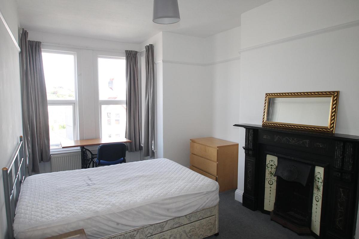 fifth student bedroom with double bed, chest of drawers, bedside table, desk with blue office chair in front of window and fireplace