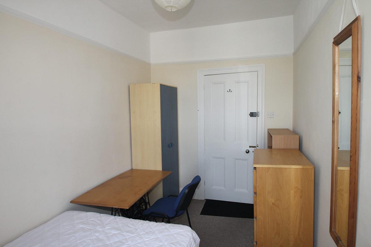 sixth student bedroom with double bed, two door wardrobe, desk with blue chair, chest of drawers and shelving unit and full length mirror