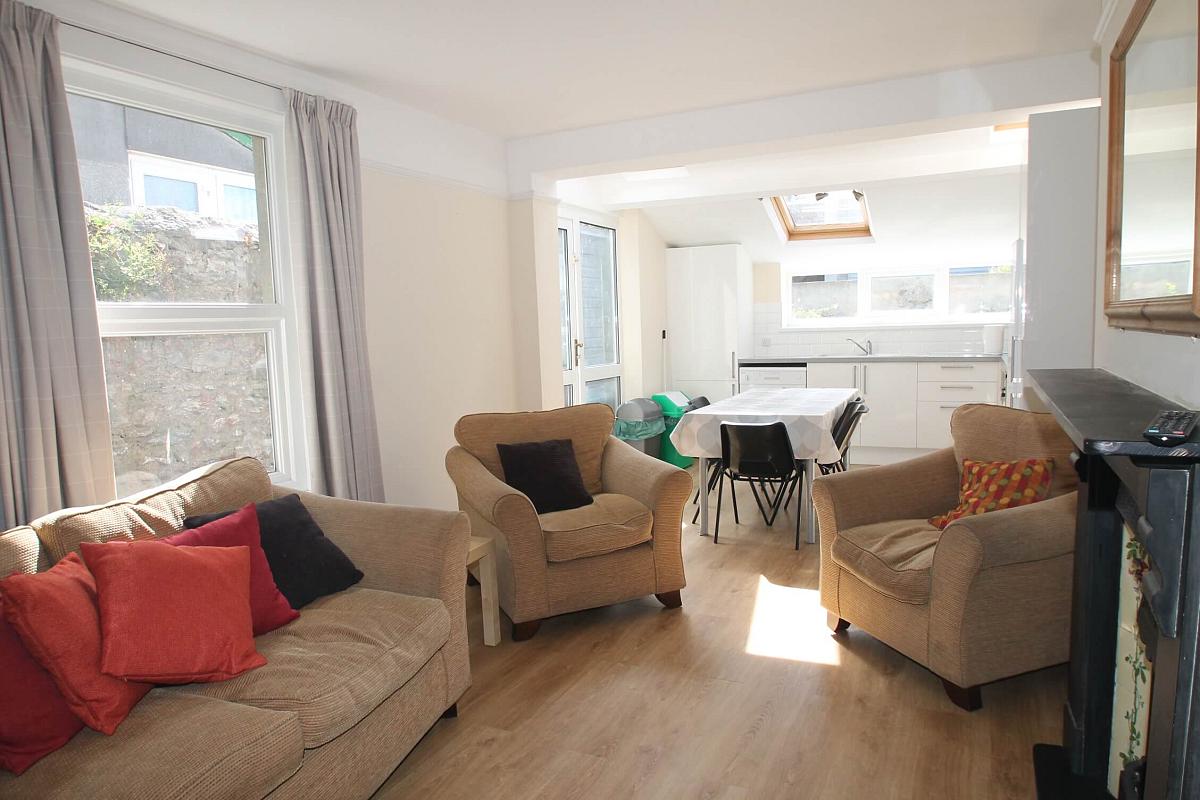 Living area with two-seater sofa, two armchairs, leading to kitchen area