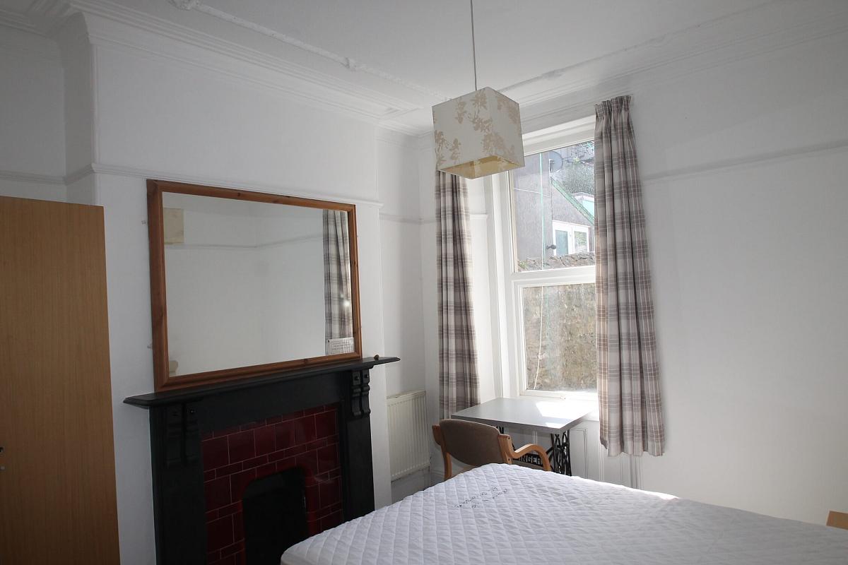 second student room with double bed, two door wardrobe, bedside table, desk with chair and large mirror above fireplace