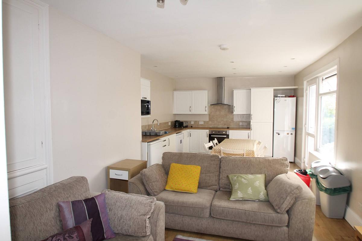 living area with two double sofas and coffee table, leading into open kitchen with large dining table and six dining chairs