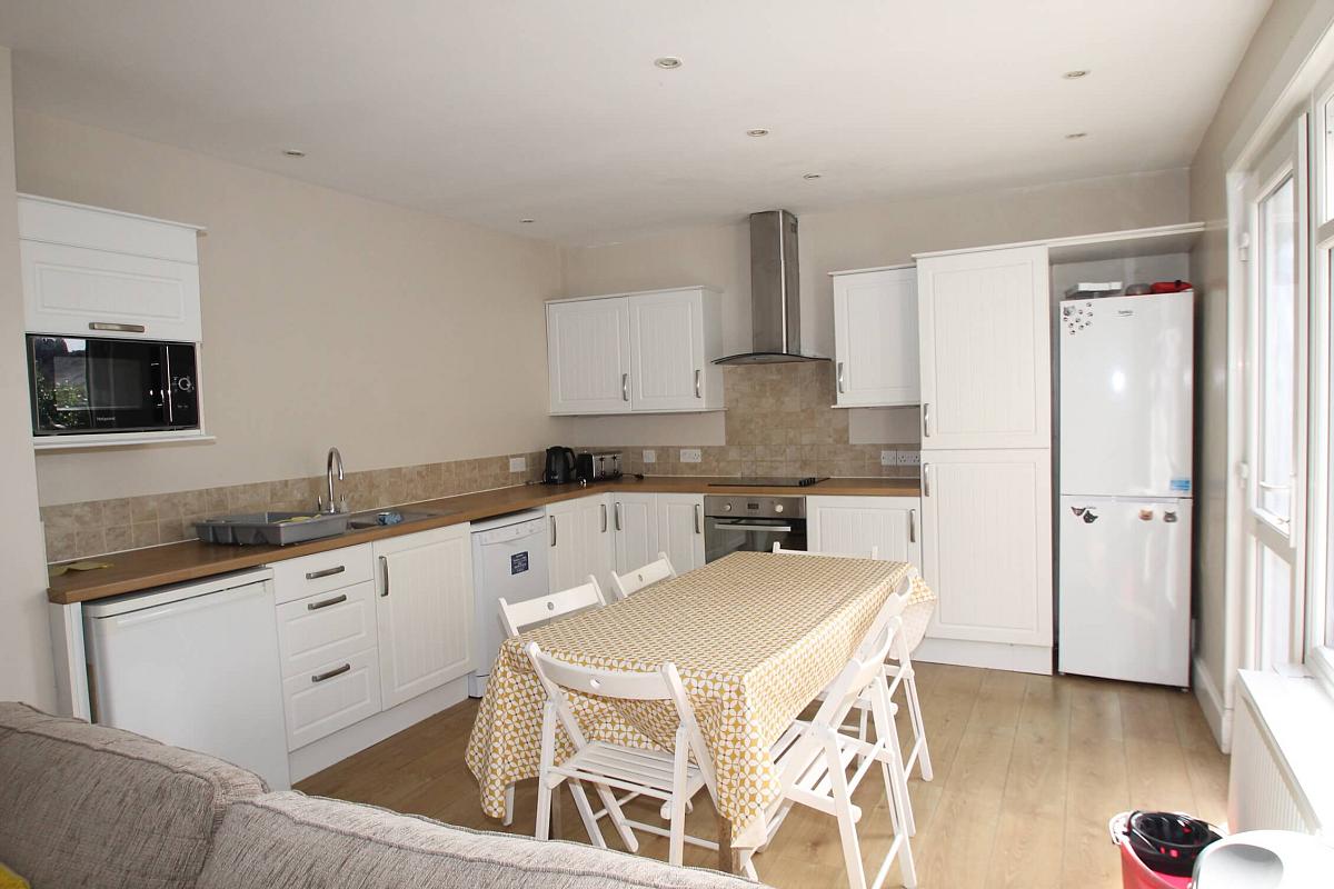 shared kitchen with fridge freezer, induction hob and cooker, microwave, dishwasher and large dining table in the middle of the room with six dining chairs