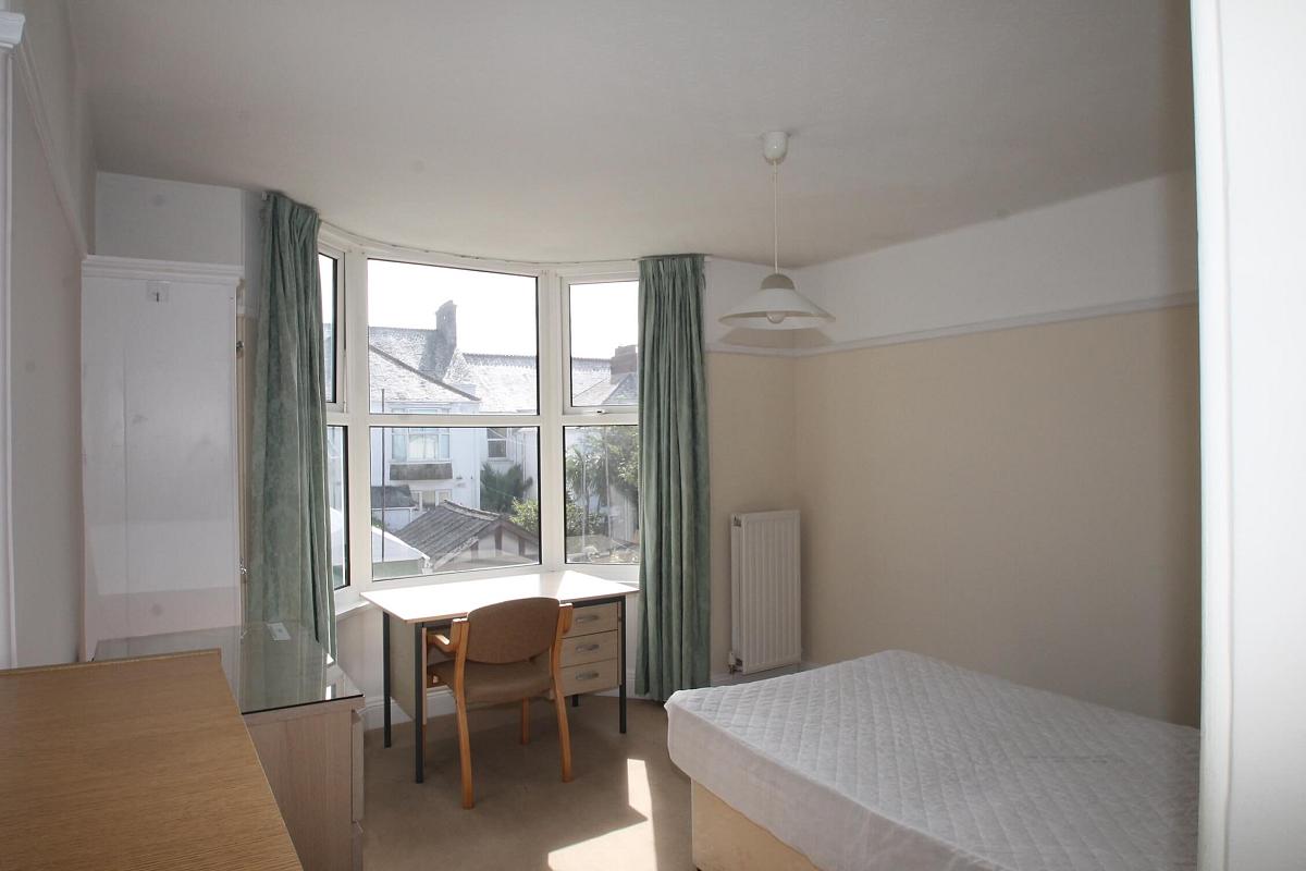 Third student room with double bed, chest of drawers, two door wardrobe and desk with chair in front of bay windows