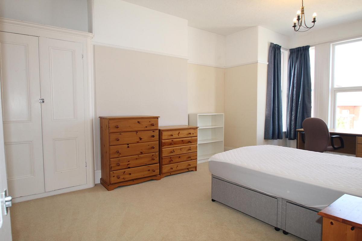 Fifth student bedroom with double bed, two chest of drawers, built-in wardrobe, shelving unit, bedside table and desk with office chair in front of window