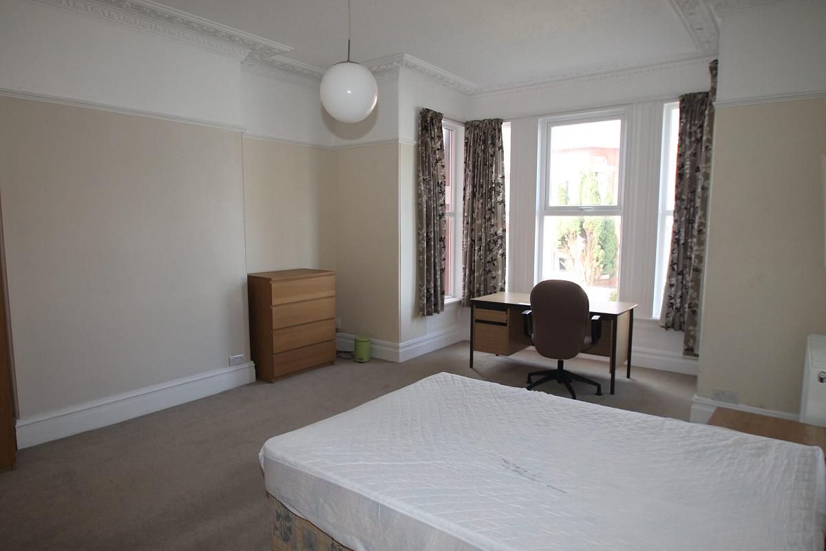 Large first student bedroom with double bed, chest of drawers, bedside table, desk with office chair in front of large bay windows
