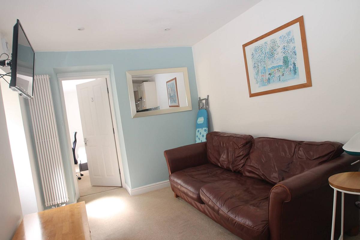 living area with large brown leather two-seater sofa, coffee table, wall mounted tv, small breakfast bar, wall mounted mirror and entrance to third student room