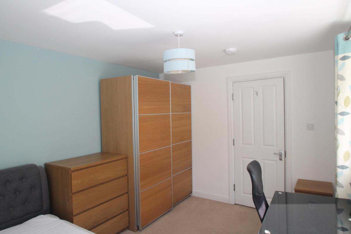 third student bedroom with double bed, two door wardrobe, chest of drawers, bedside table and glass desk with black office chair
