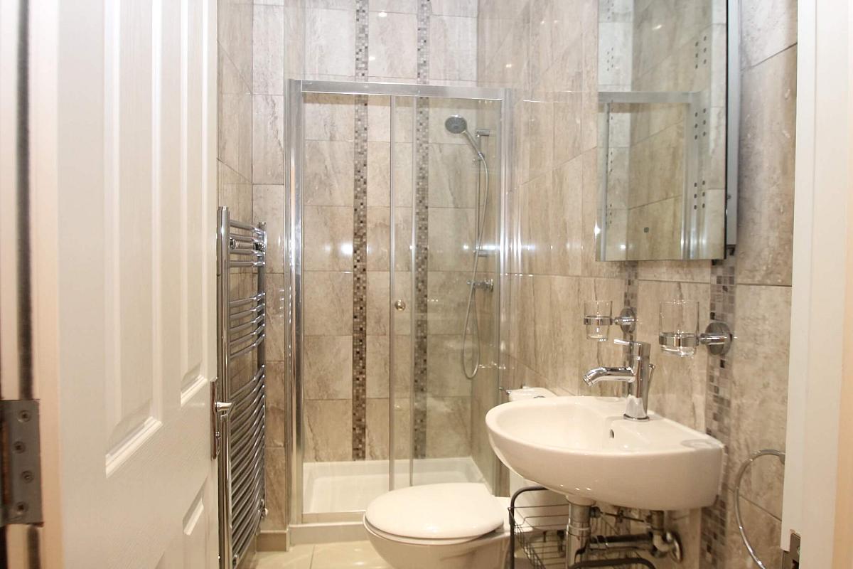 Shared bathroom with shower, towel rack radiator and light up mirror mounted above sink