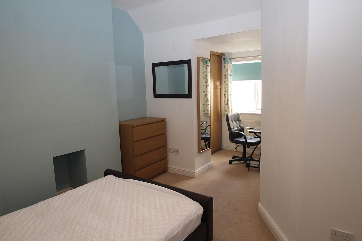 second student room with double bed, two bedside tables, chest of drawers, wall mounted mirror. full length mirror, desk with office chair and two door wardrobe