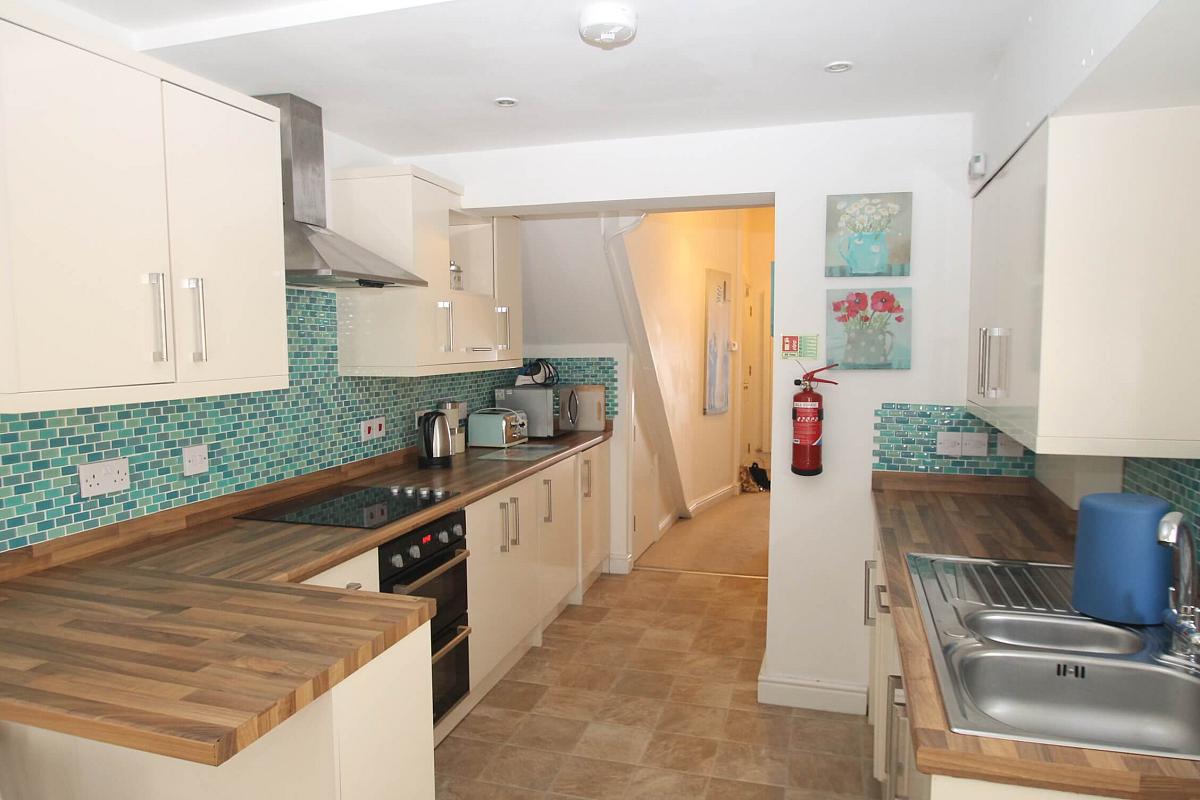 kitchen with hobs and cooker, double sink. microwave and hallway leading to front of the flat