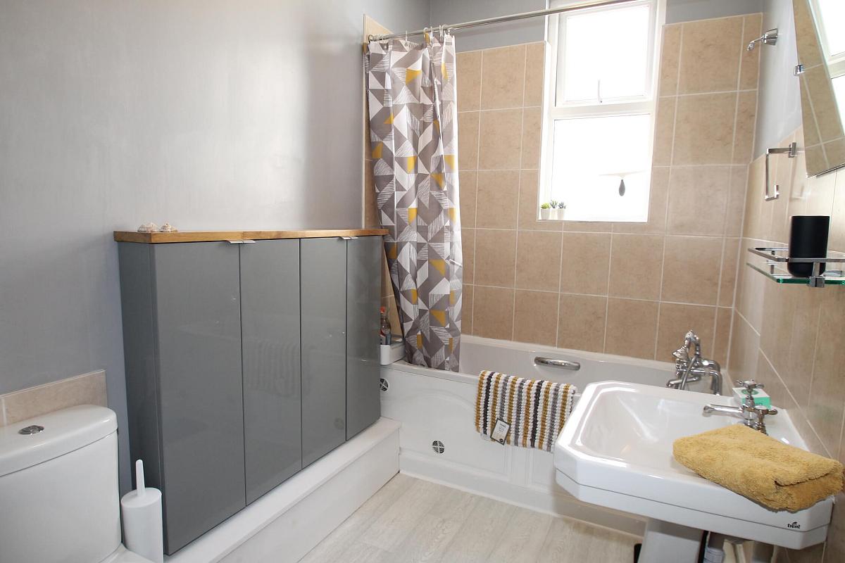 shared bathroom with bath and with shower head, grey cupboard, shelf and mirror mounted above sink
