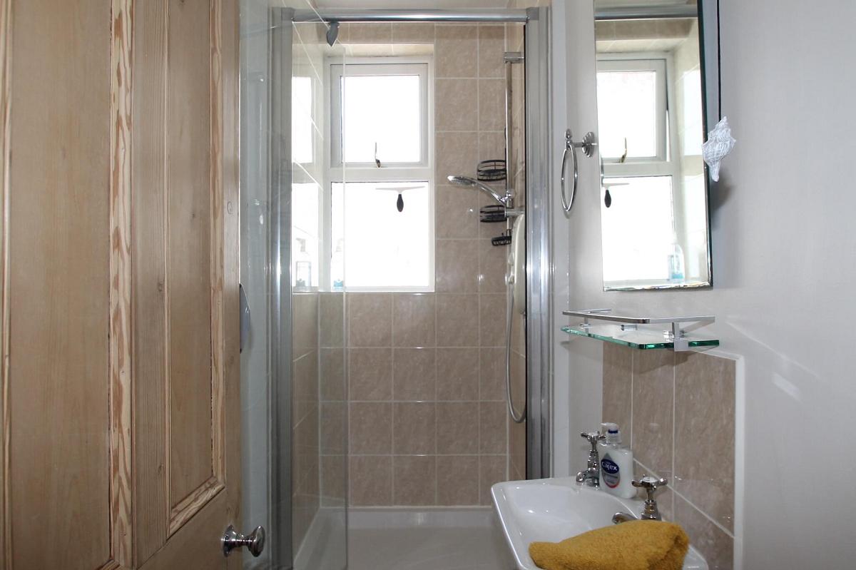 Shared bathroom with shower, shelves and mirror mounted above sink