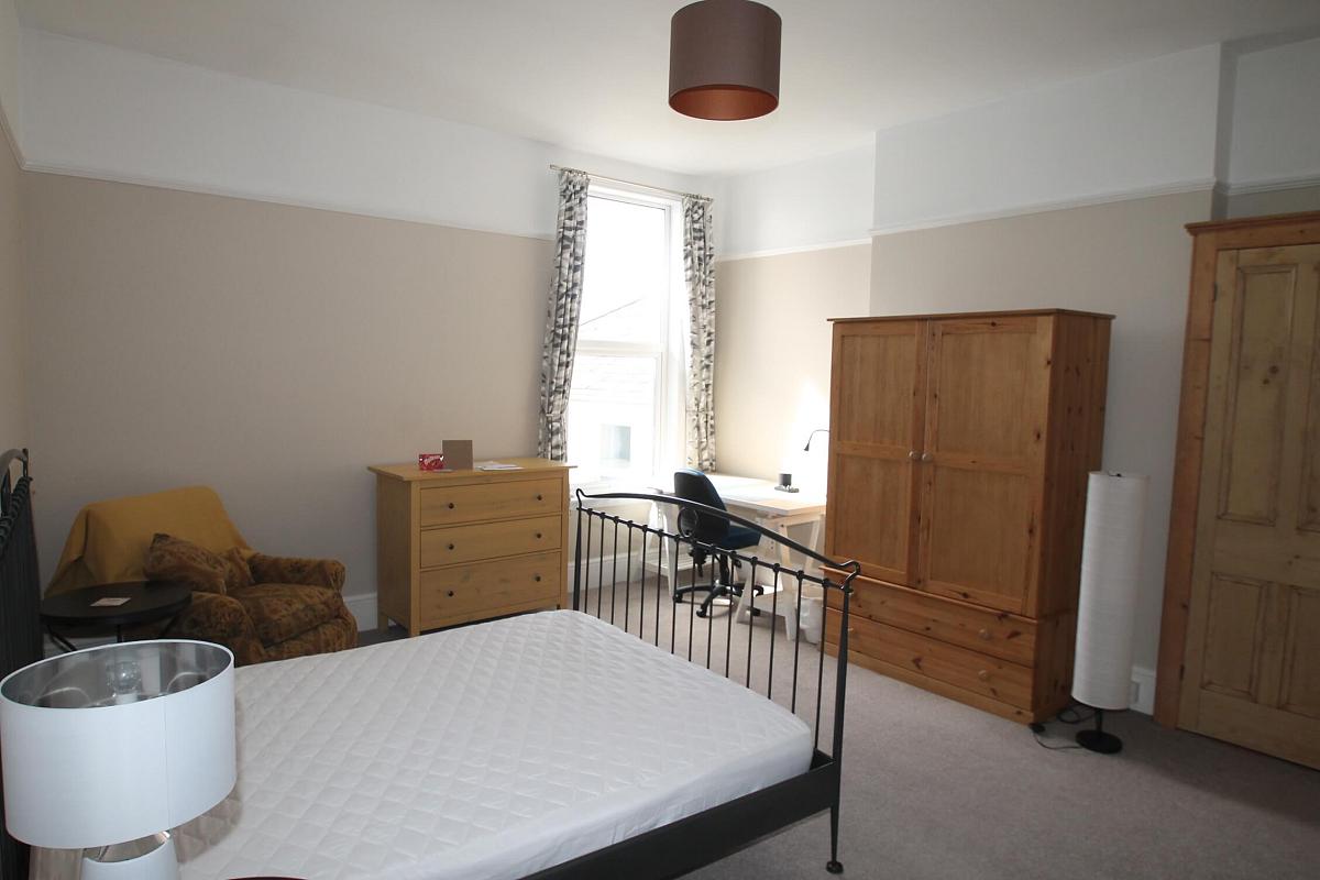 fourth student room with double bed, chest of drawers, two door wardrobe, bedside table, armchair and desk with blue office chair