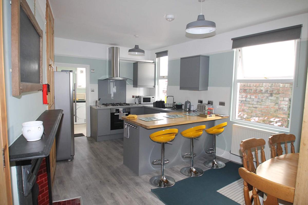 Open kitchen and dining area with gas hobs and cooker, dishwasher, small breakfast bar with three yellow barstools and dining table