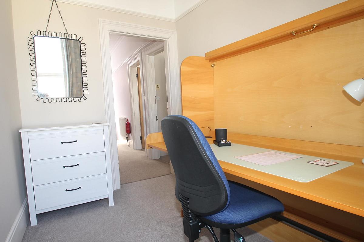 Office room with desk and blue office chair, white chest of drawers and mirror hanging on wall
