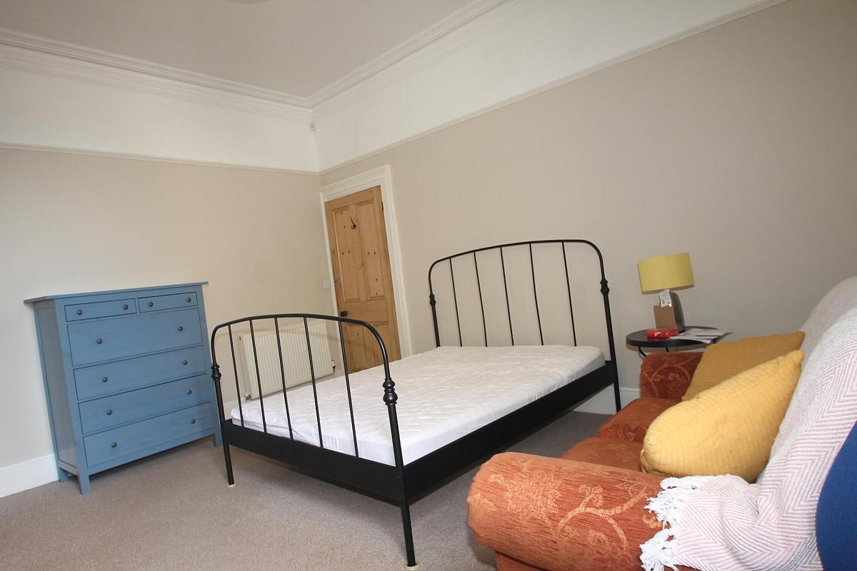 First student bedroom with double bed, bedside table, two-seater sofa, and blue chest of drawers