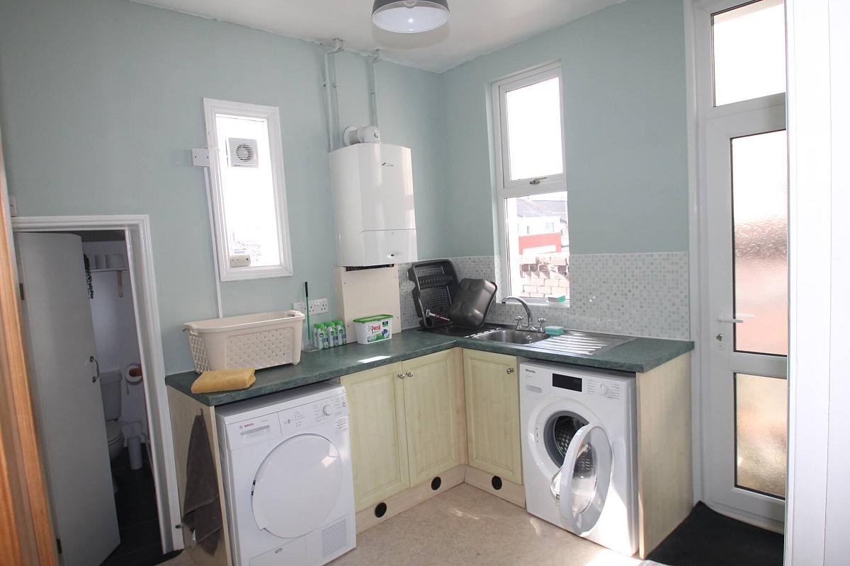 Utility room with washing machine and tumble dryer with sink, leading to separate WC