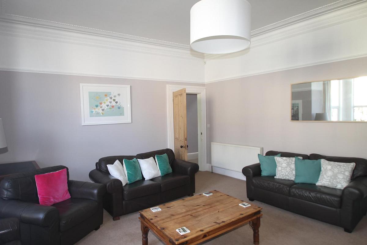 shared living room with three leather two-seater sofas, two arm chairs, coffee table and large mirror mounted on wall