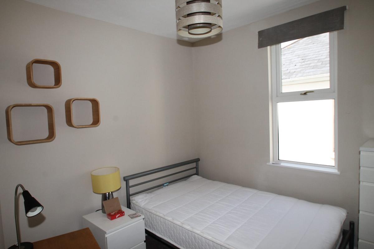 third student room with double bed, bedside table, tall chest of drawers, desk and three square feature shelves