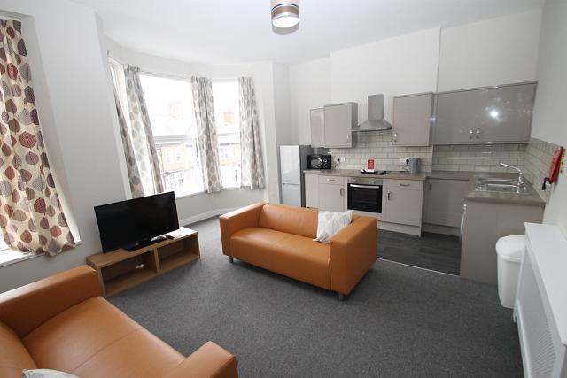 open kitchen and living area with two yellow sofas, television on tv stand, kitchen with fridge freezer, induction hobs and cooker and large bay windows