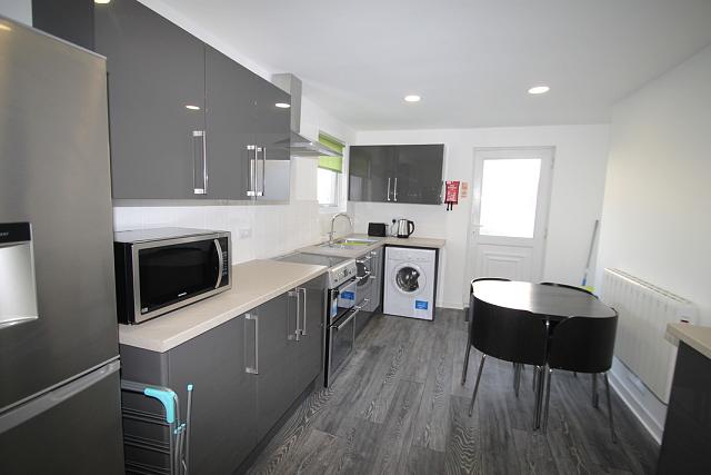 Shared kitchen with fridge freezer, washer/dryer, induction hobs and cooker, microwave and black dining table with four black dining chairs
