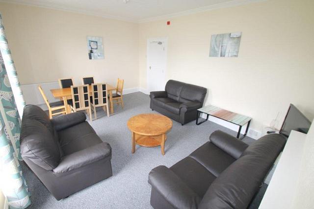Shared living room with three black two-seater sofas, six-seater dining table and two coffee tables