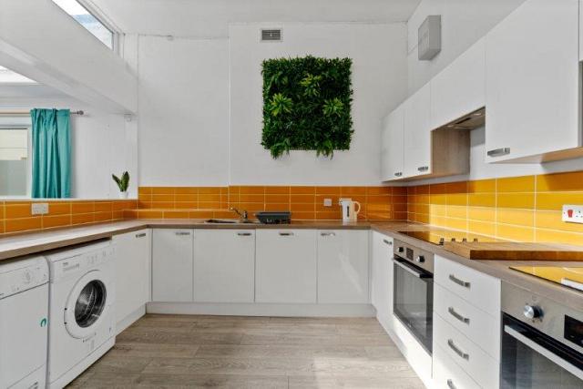 yellow tiled kitchen with two induction hobs and cooker, washing machine, tumble dryer and sink