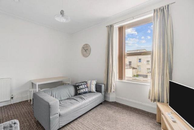 living room with large grey sofa, dining table with two stools and television on tv stand