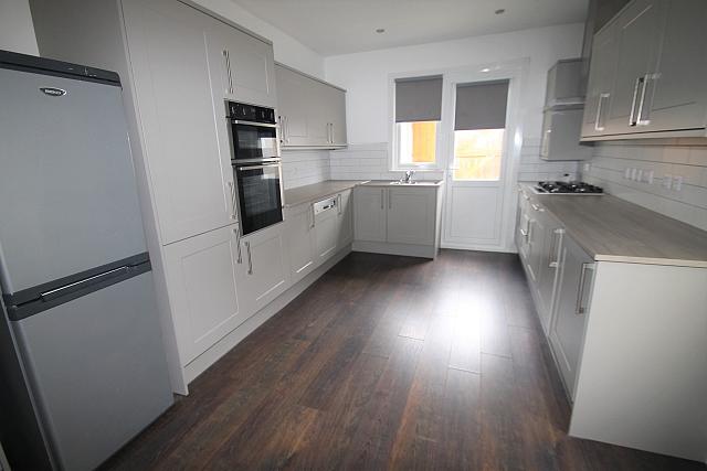 White shared kitchen with fridge freezer, hob and cooker, entrance to back garden
