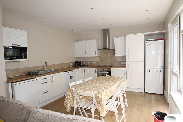 shared kitchen with fridge freezer, induction hob and cooker, microwave, dishwasher and large dining table in the middle of the room with six dining chairs